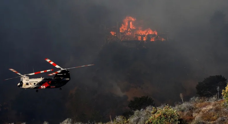 Sebuah helikopter terbang di dekat sebuah rumah yang terbakar saat Kebakaran Palisades berkobar di Mandeville Canyon, Los Angeles, California (Shannon Stapleton/Reuters)